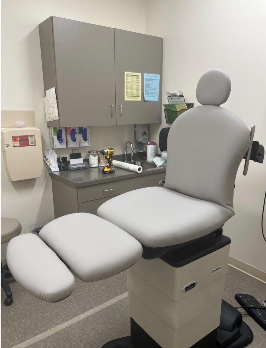 Light-gray upholstered examination table with adjustable headrest and padded leg supports